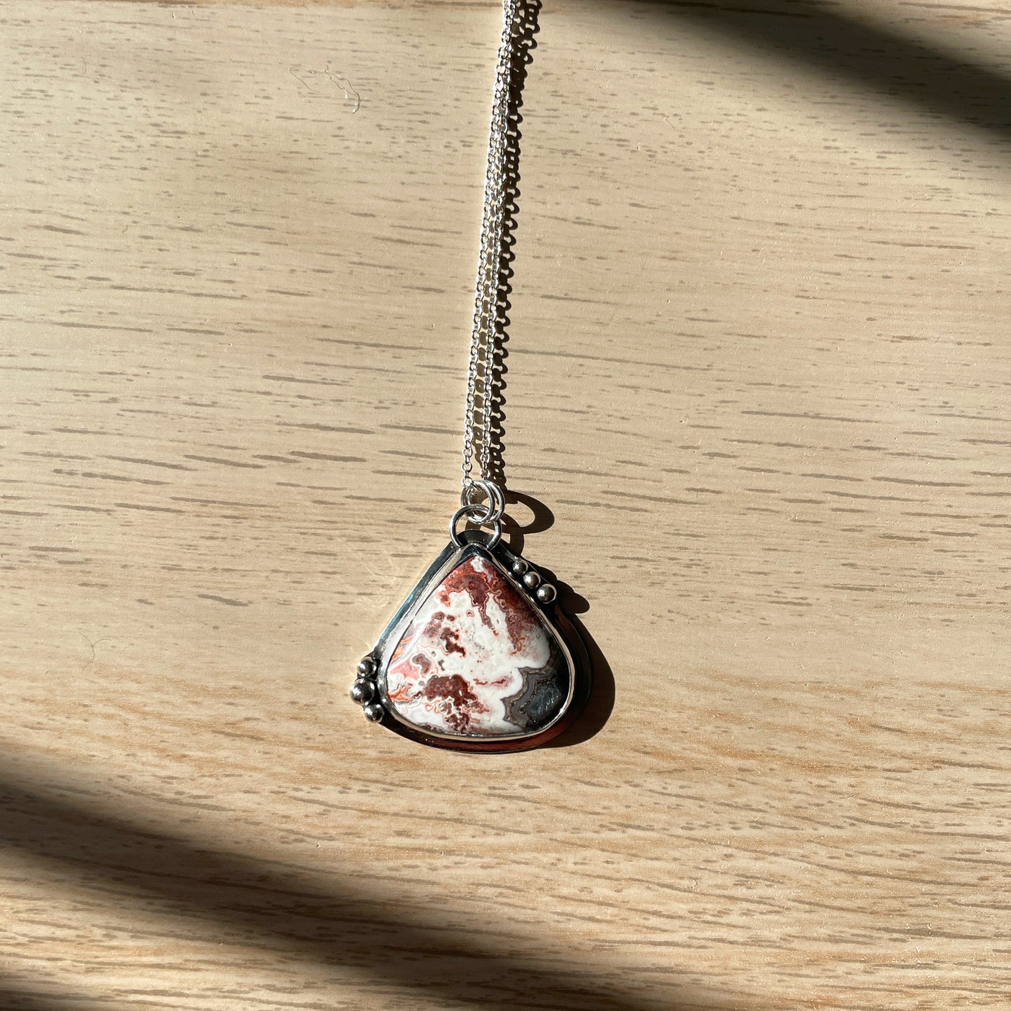 Teardrop-shaped silver pendant on a chain against a wooden background